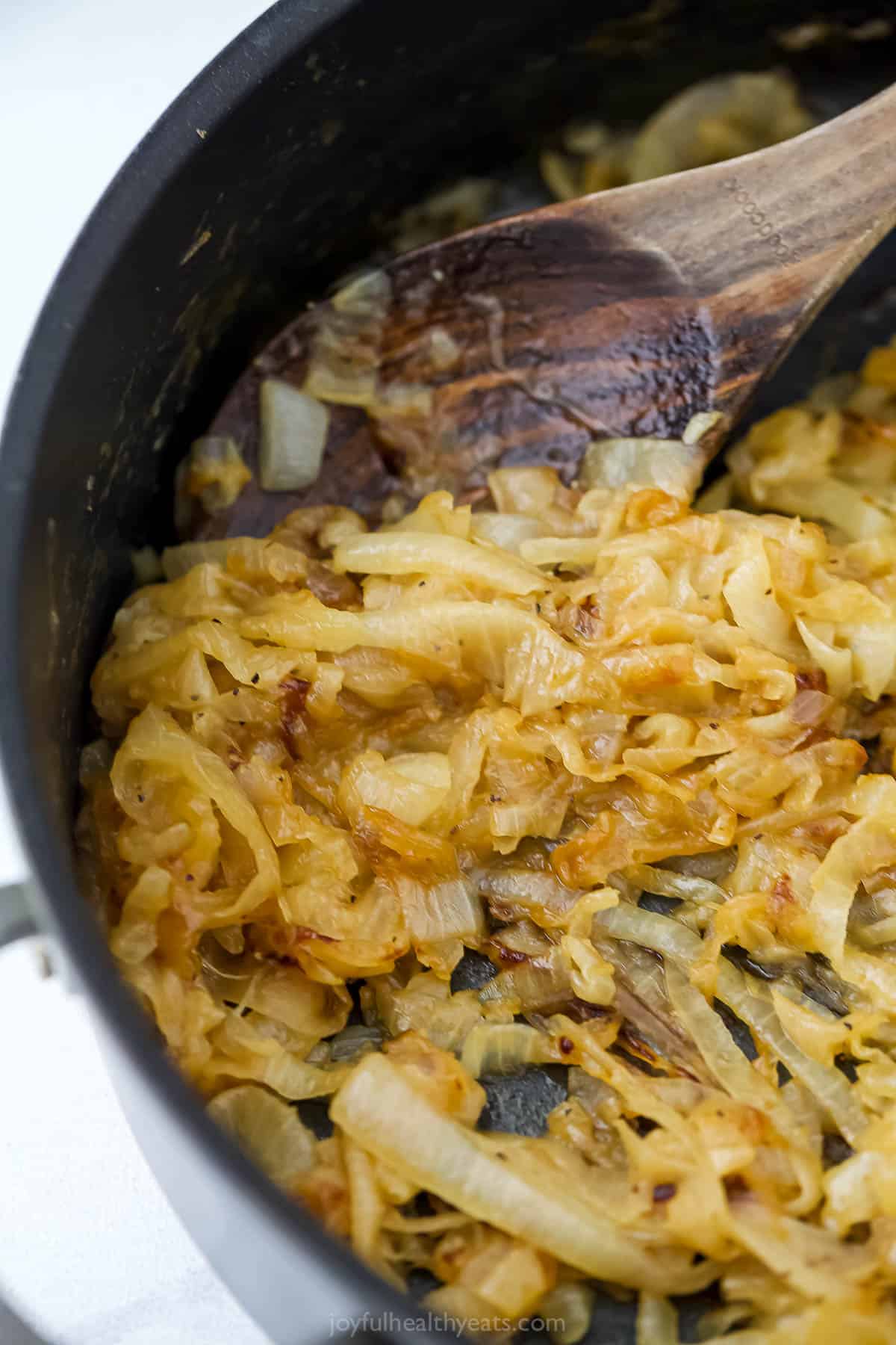 Wooden spoon stirring caramelized onions in skillet.
