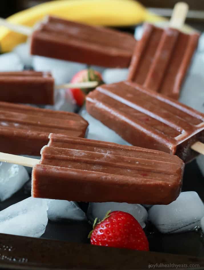 Six fruity fudge pops beside fresh strawberries and a banana