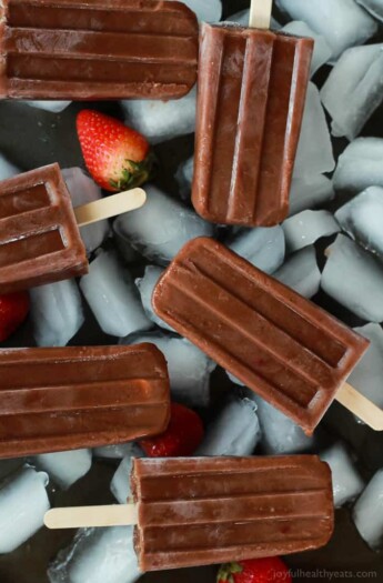 Six dairy-free popsicles on top of a layer of ice and fresh strawberries