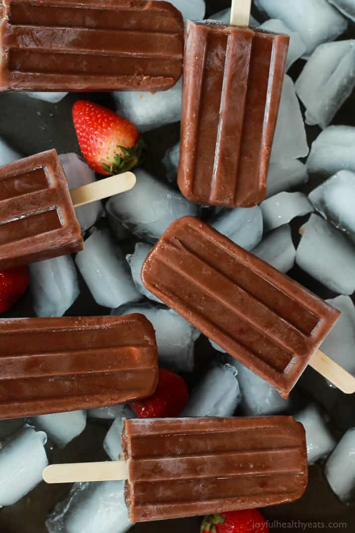 Six dairy-free popsicles on top of a layer of ice and fresh strawberries