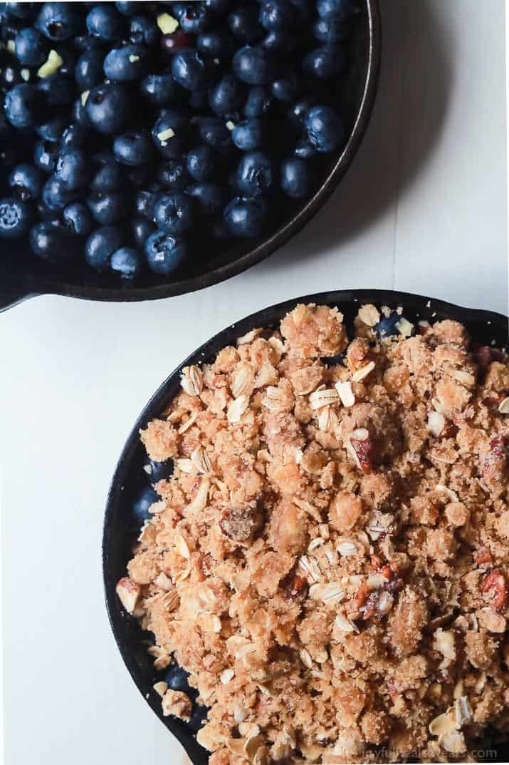 Blueberries inside of a skillet beside a skillet full of blueberry filling and pecan topping