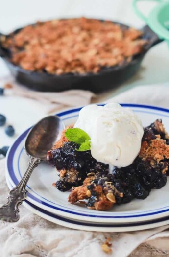 A serving of berry crisp on a plate with the remaining crisp inside of a pan in the background