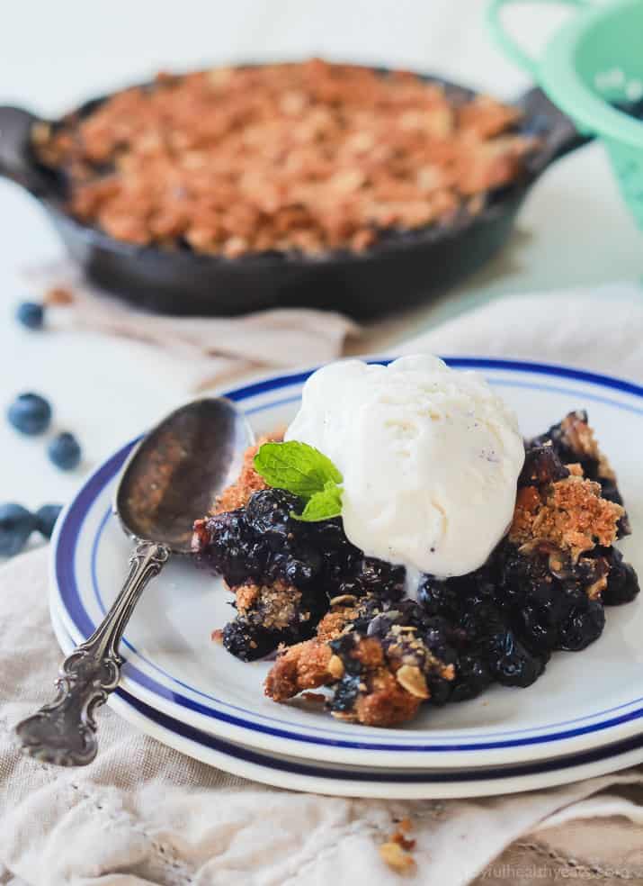 A serving of berry crisp on a plate with the remaining crisp inside of a pan in the background