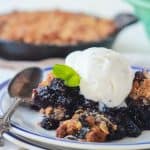 A ginger blueberry crisp on top of a stack of two plates with a metal spoon beside it