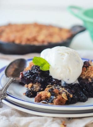 A ginger blueberry crisp on top of a stack of two plates with a metal spoon beside it