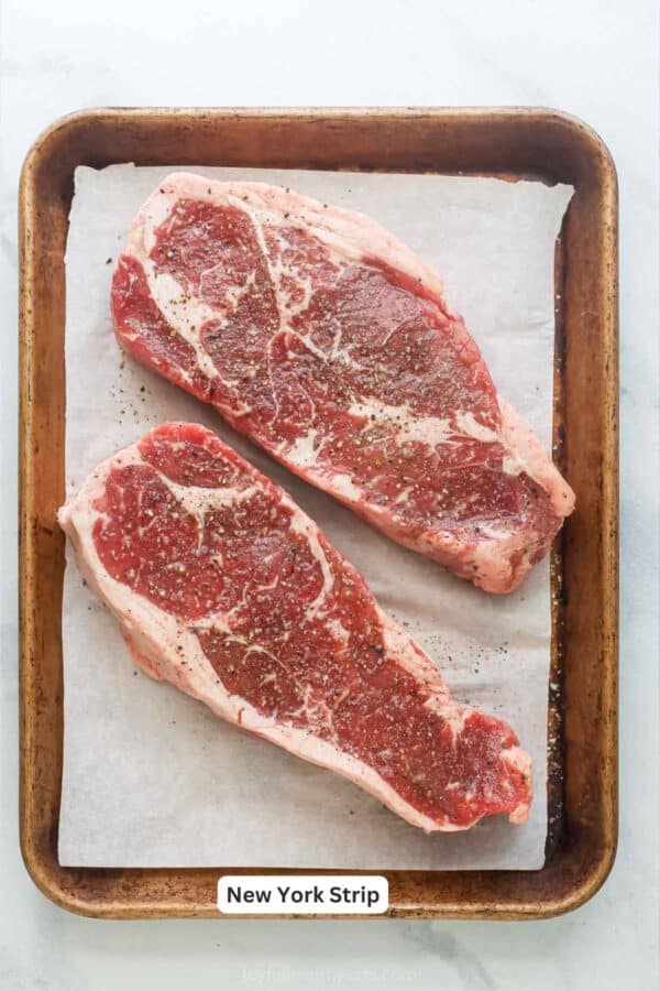 Two New York strip steaks on sheet pan.