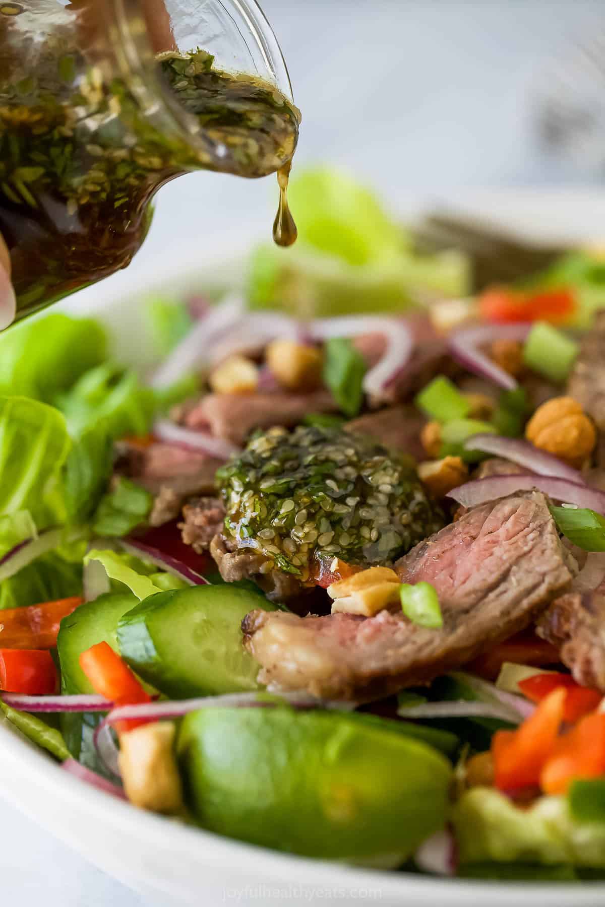 Pouring sesame vinaigrette onto Thai steak salad.
