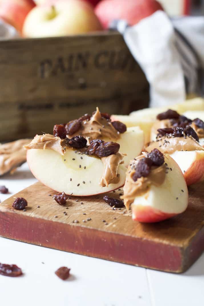 Apple wedges with peanut butter, dried cranberries, and chia seeds on a wooden cutting board