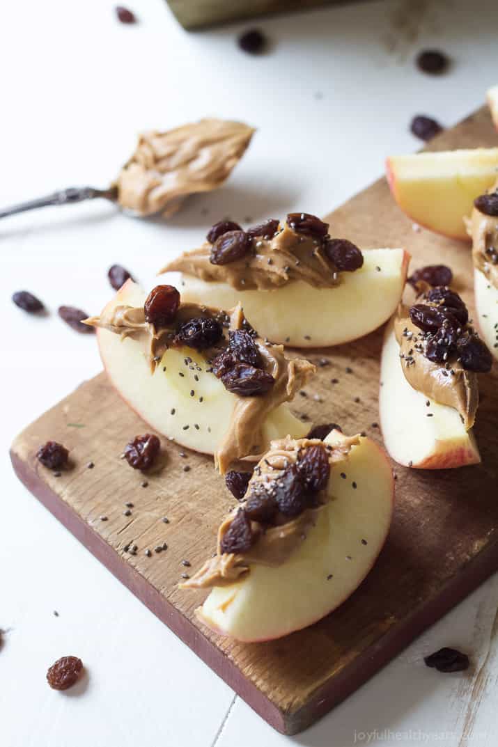 Overhead view of apple wedges with peanut butter, dried cranberries and chia seeds on a wooden cutting board