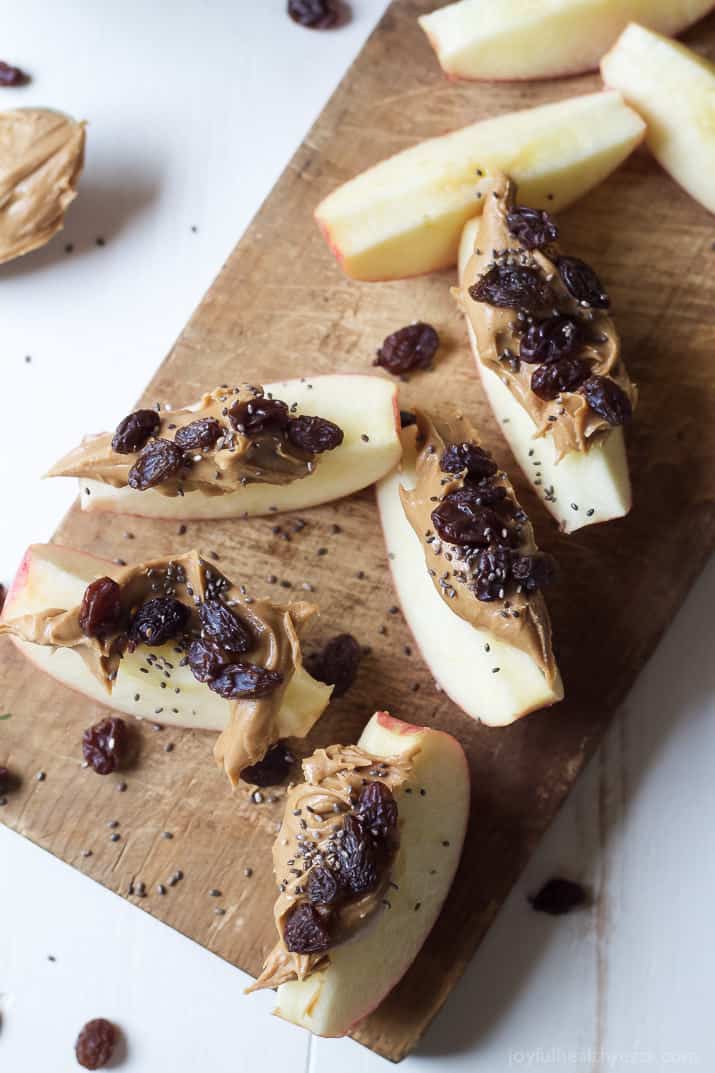 Top view of apple wedges with peanut butter, dried cranberries and chia seeds on a wooden cutting board