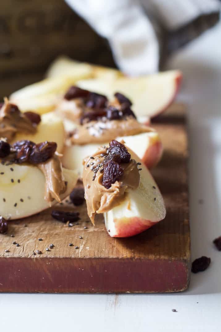 Apple slices with peanut butter, dried fruit, and chia seeds on a wooden cutting board