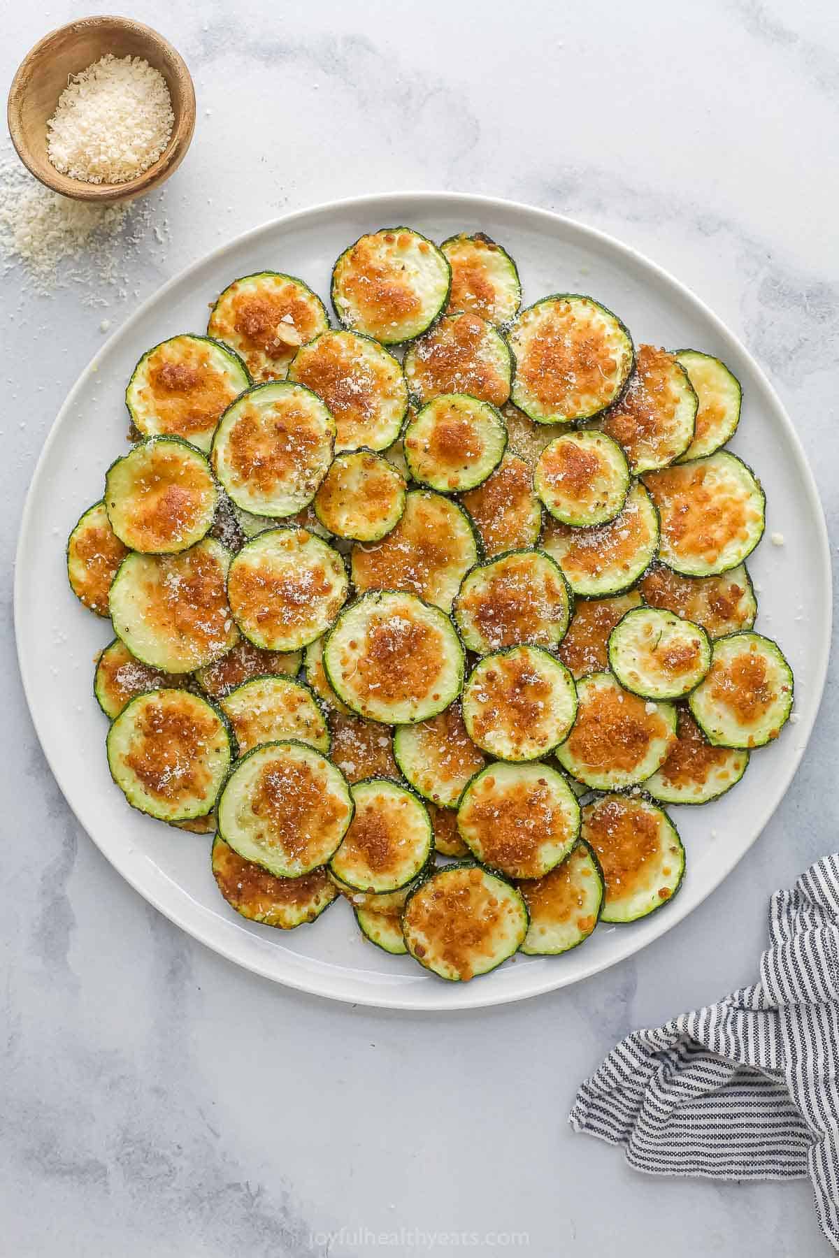 These quick and easy air fryer zucchini chips have a crispy texture and garlic Parmesan flavor that makes them totally irresistible! Overhead view of Parmesan garlic air fryer zucchini chips on plate