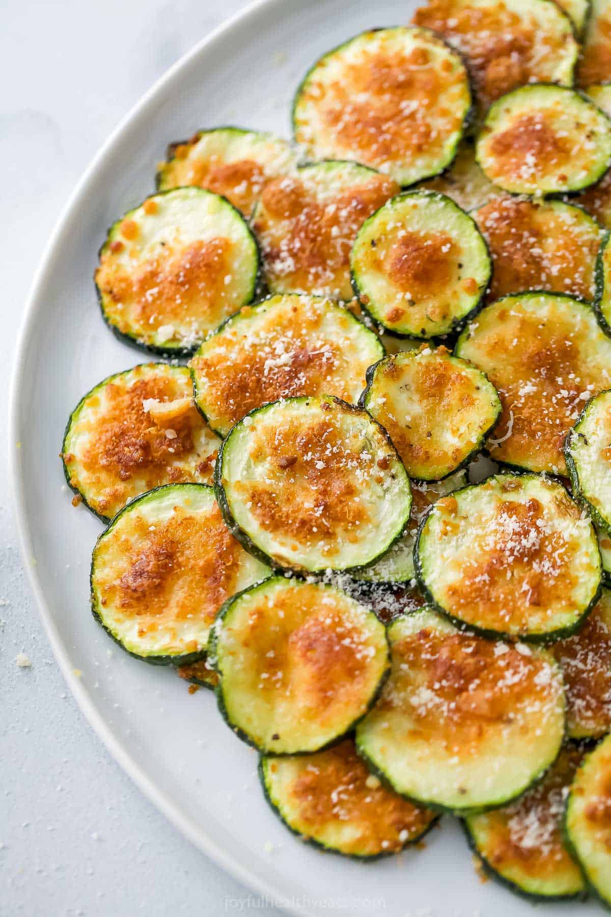 These quick and easy air fryer zucchini chips have a crispy texture and garlic Parmesan flavor that makes them totally irresistible! Overhead view of plate of air fryer zucchini chips