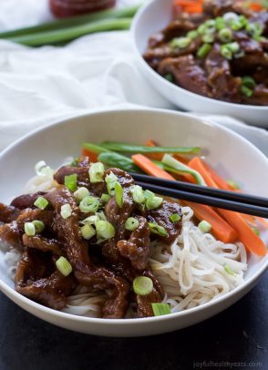 Sweet and spicy strips of flank steak in a shallow bowl with veggies, noodles and a pair of black chopsticks