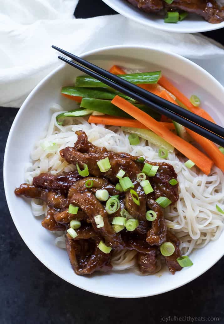 A shallow bowl filled with Asian-style flank steak, rice noodles, carrots, cucumbers and a pair of chopsticks