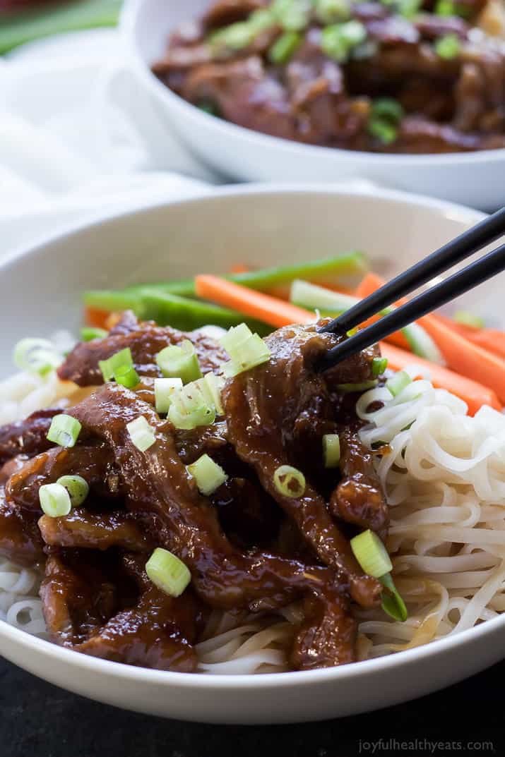 A bowl of honey sriracha Mongolian beef over rice noodles with a second bowl in the background