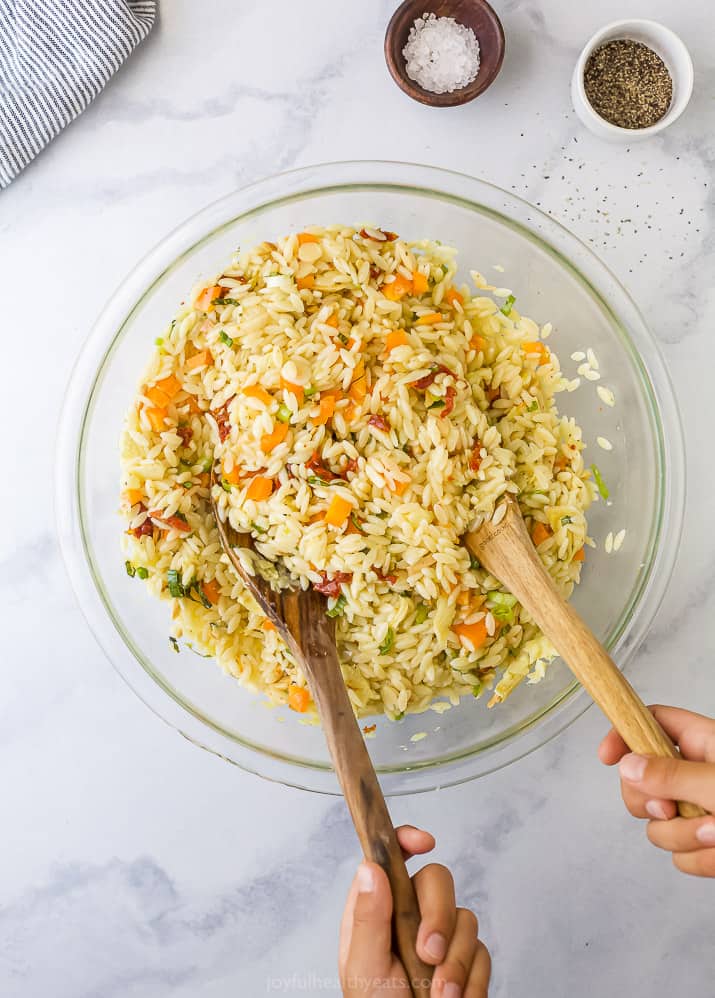 Two Hands Scooping Wooden Spoons in a Bowl of Pasta Salad