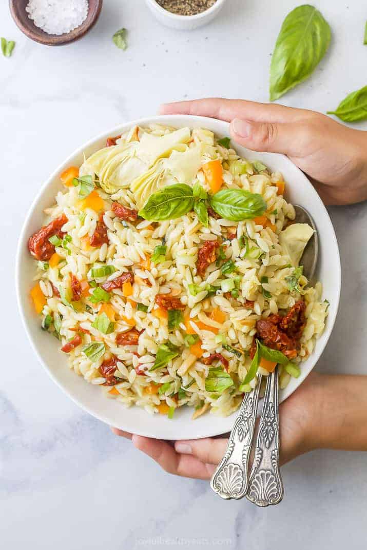 Two Hands Holding a Bowl of Mediterranean Salad with Two Spoons Inside