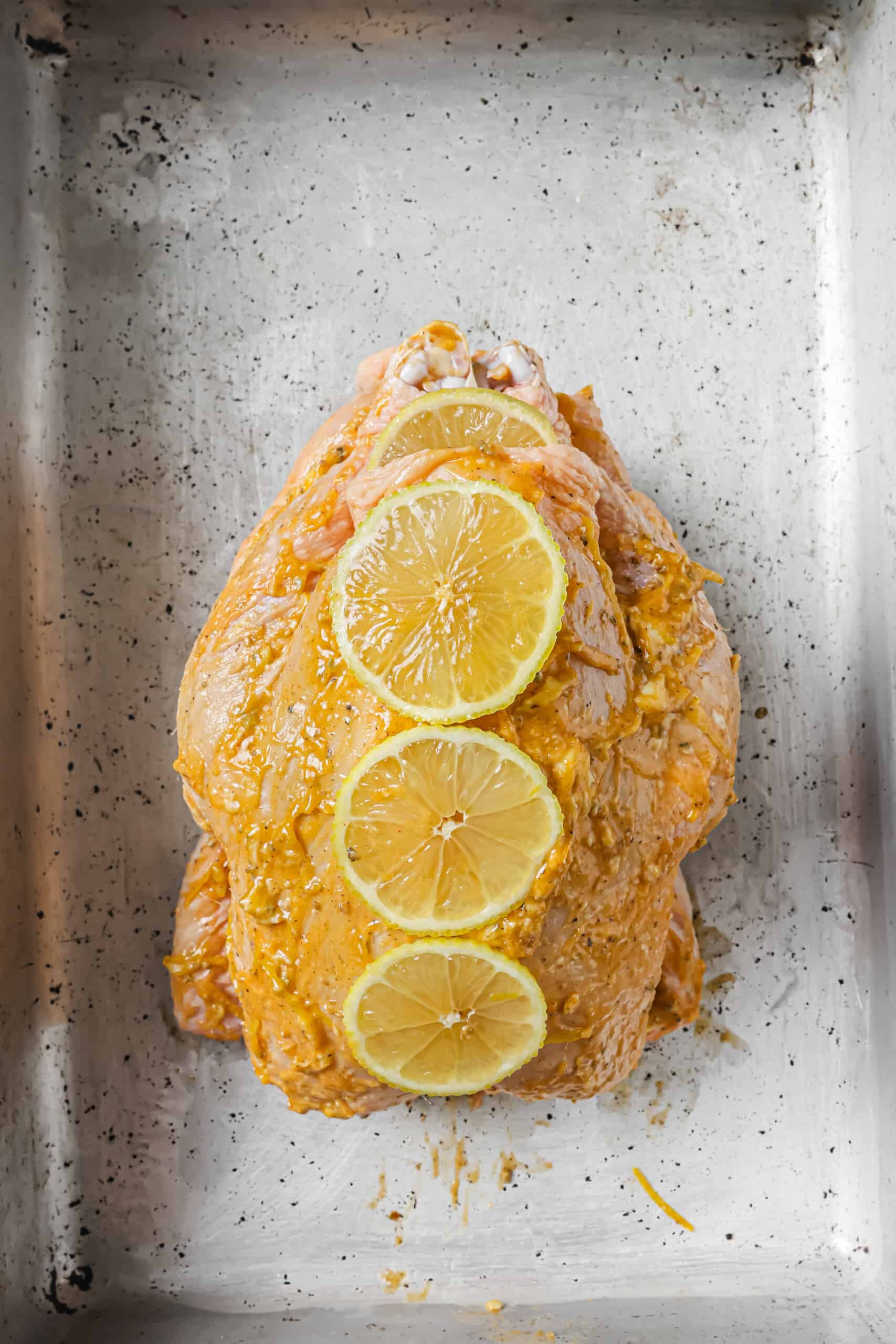Placing lemon slices on the chicken rubbed with flavored butter. 