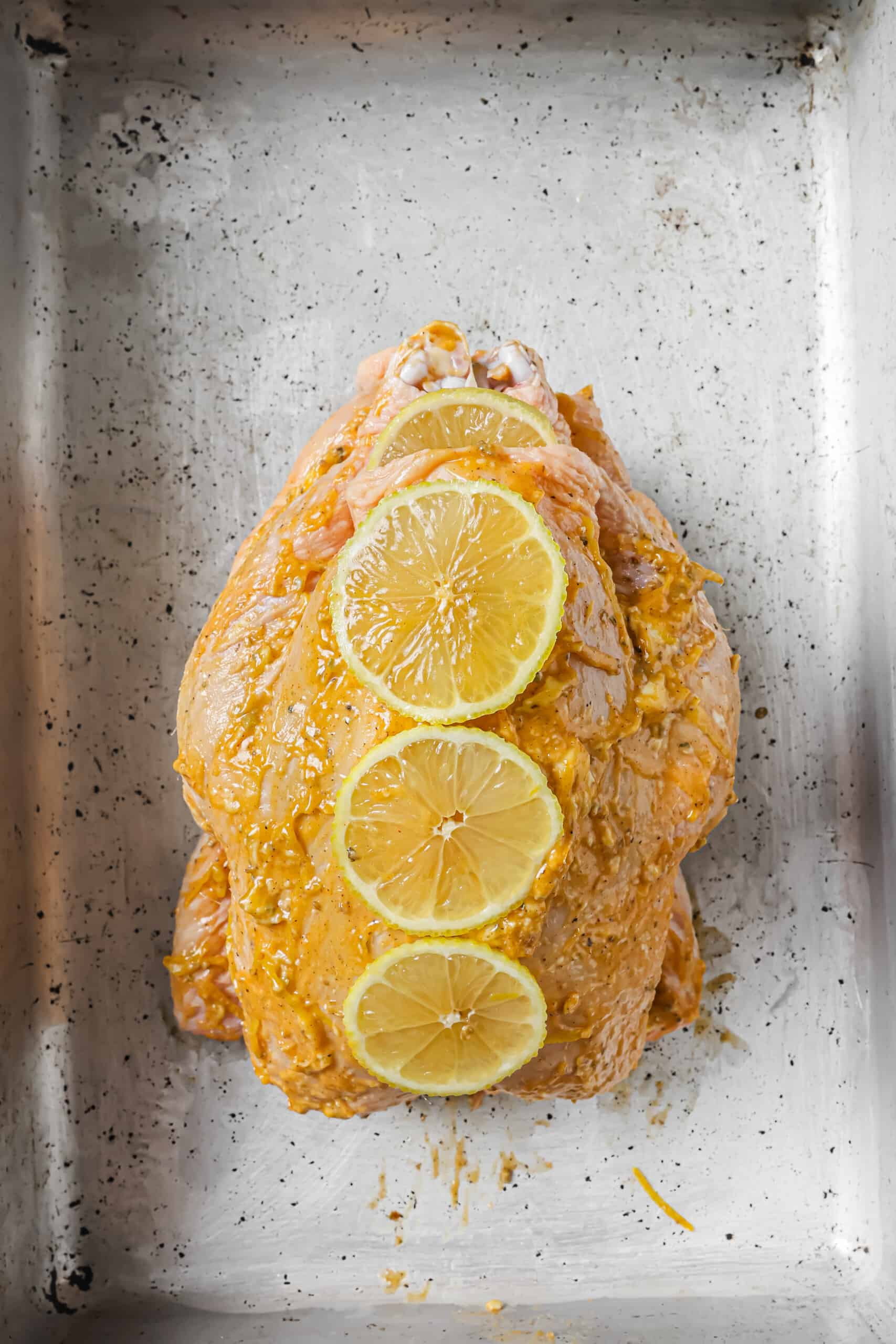 With crispy skin and zesty butter, this bake-and-forget roasted chicken recipe will be a weeknight favorite! Placing lemon slices on the chicken rubbed with flavored butter.