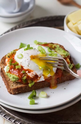 A piece of Harissa Avocado Toast Topped with Poached Egg with a fork cutting into the egg.