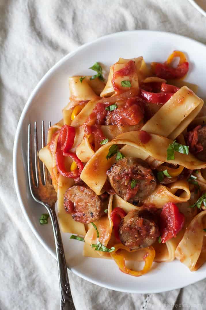 A plate of tomato, sausage and pepper pasta on top of a large cloth napkin
