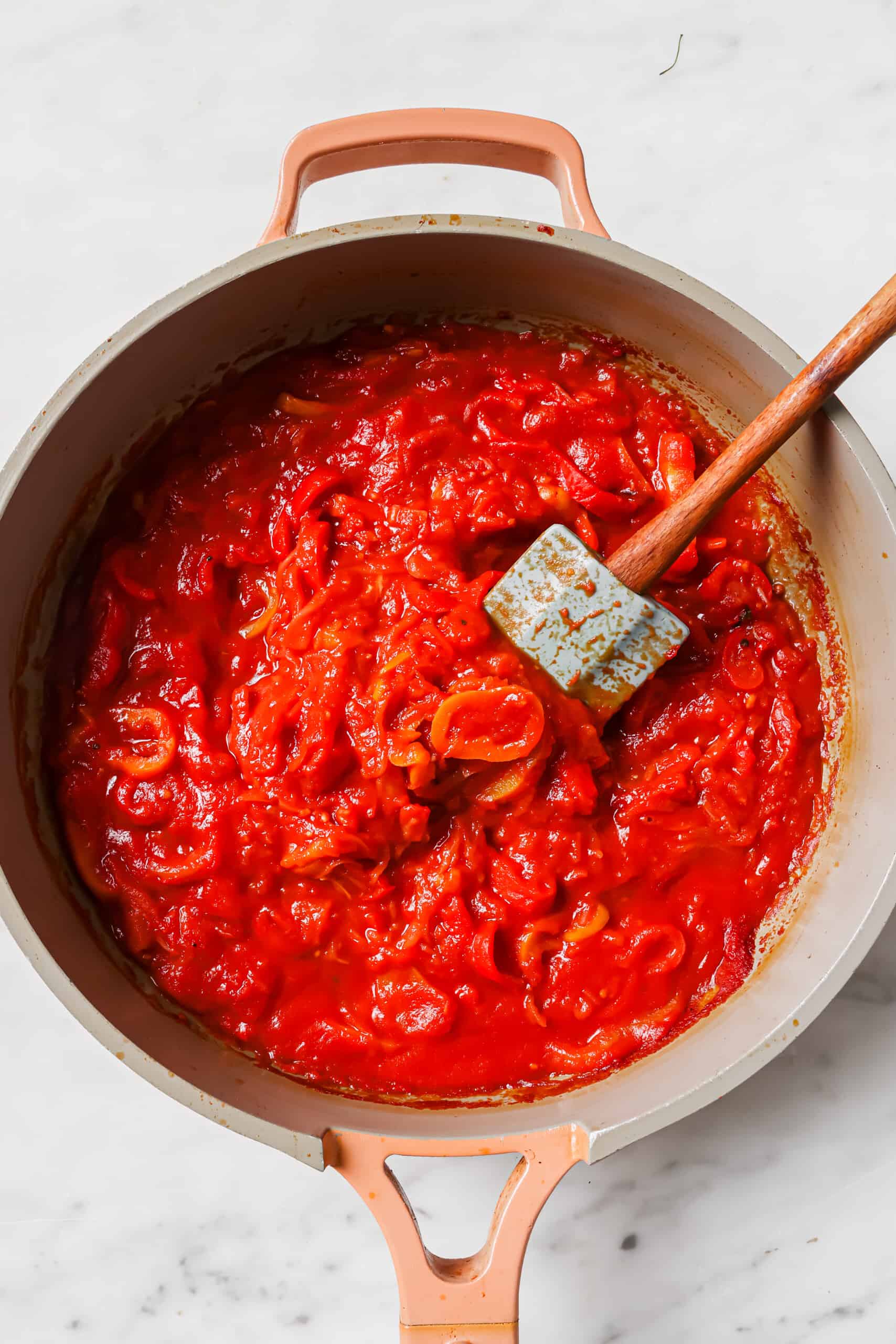 Adding the crushed tomatoes to the pan with peppers and onions. 