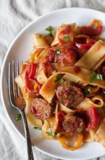 A plate of tomato, sausage and pepper pasta on top of a large cloth napkin