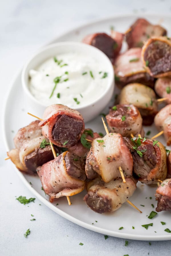 Plate of juicy tenderloin bites wrapped in bacon with a side of horseradish sauce.