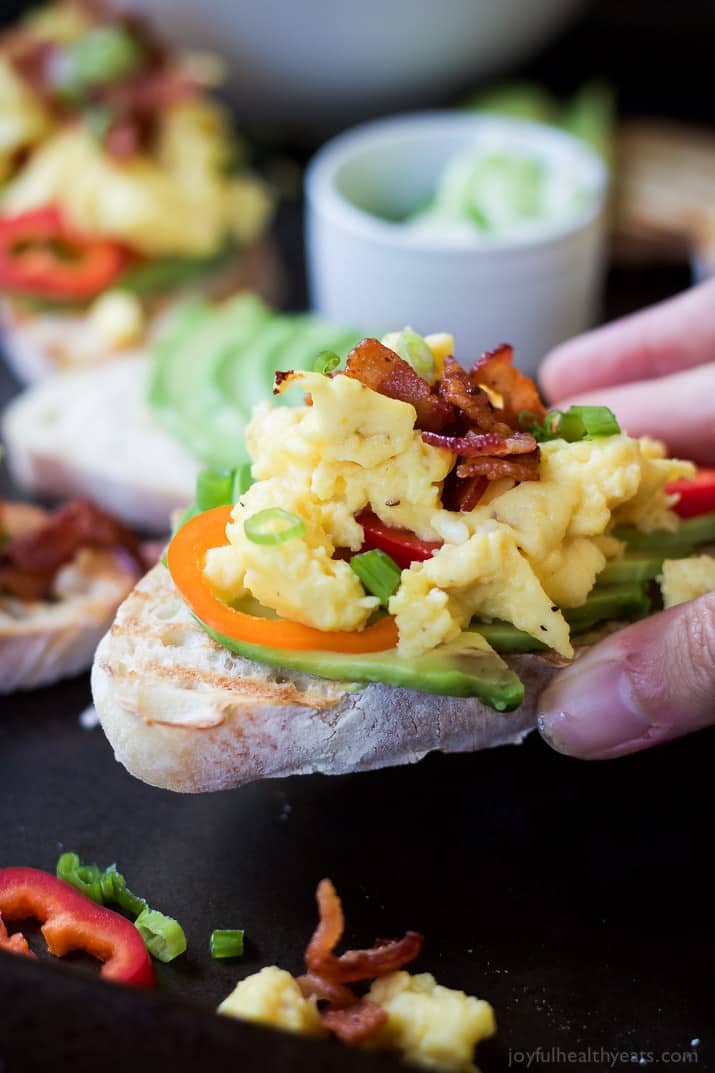 A Hand Holding a Piece of Breakfast Bruschetta on Avocado Toast with Eggs