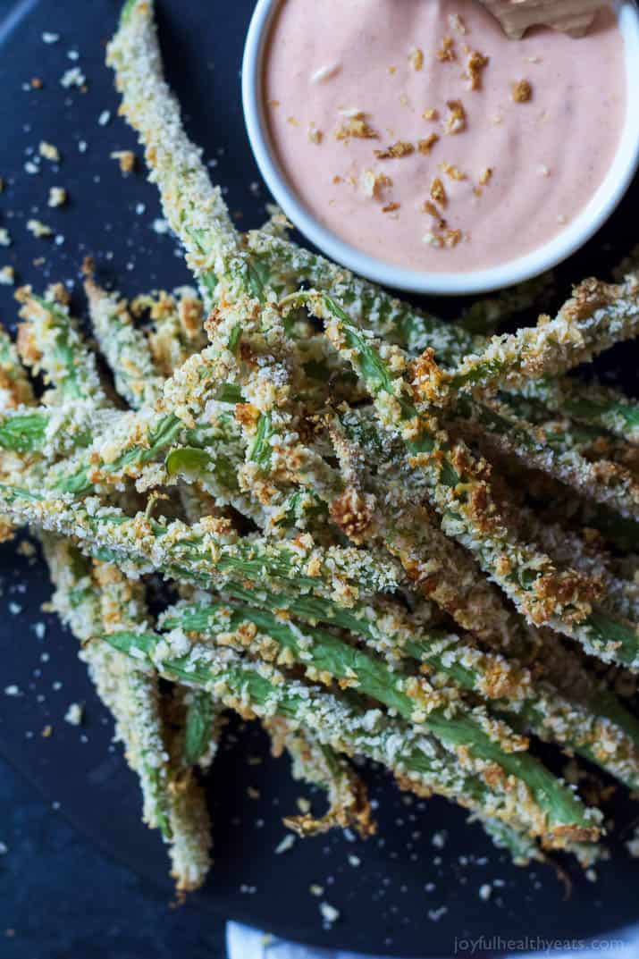 Top view of Crispy Baked Green Bean Fries with a cup of Creamy Sriracha Sauce for dipping on a plate