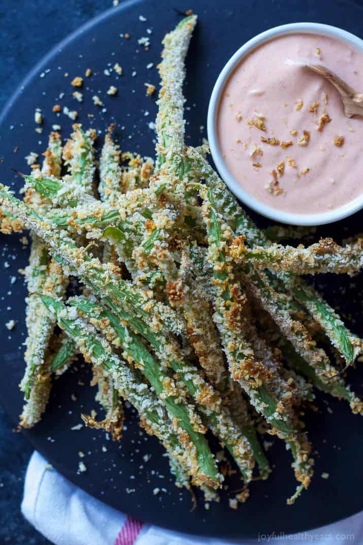 Top view of Crispy Baked Green Bean Fries with a cup of Creamy Sriracha Sauce on a plate
