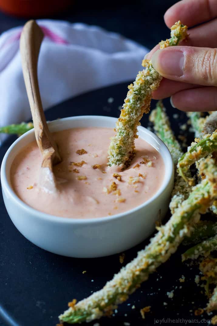 Crispy Baked Green Bean Fries being dipped into a cup of Creamy Sriracha Sauce