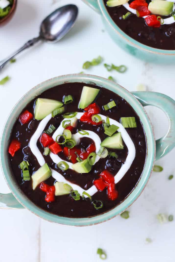 Top view of a bowl of Black Bean Soup topped with diced peppers, avocado, scallions, and a swirl of sour cream