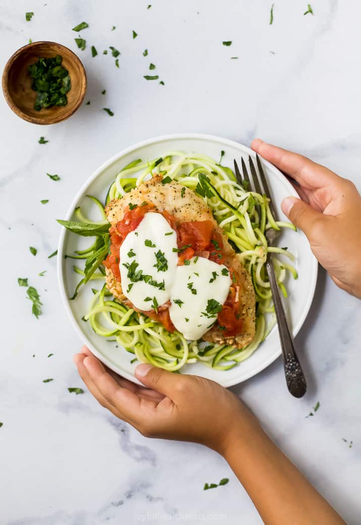 baked chicken parmesan on a bed of zucchini noodles with hands holding a plate