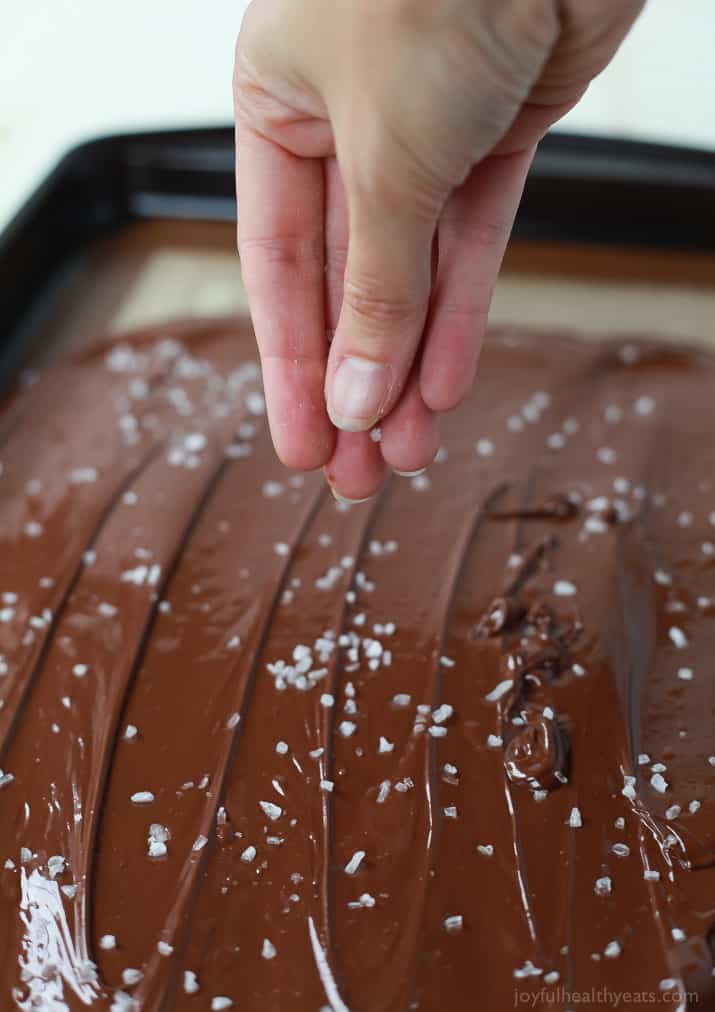 Salt being sprinkled over melted chocolate on a sheet pan
