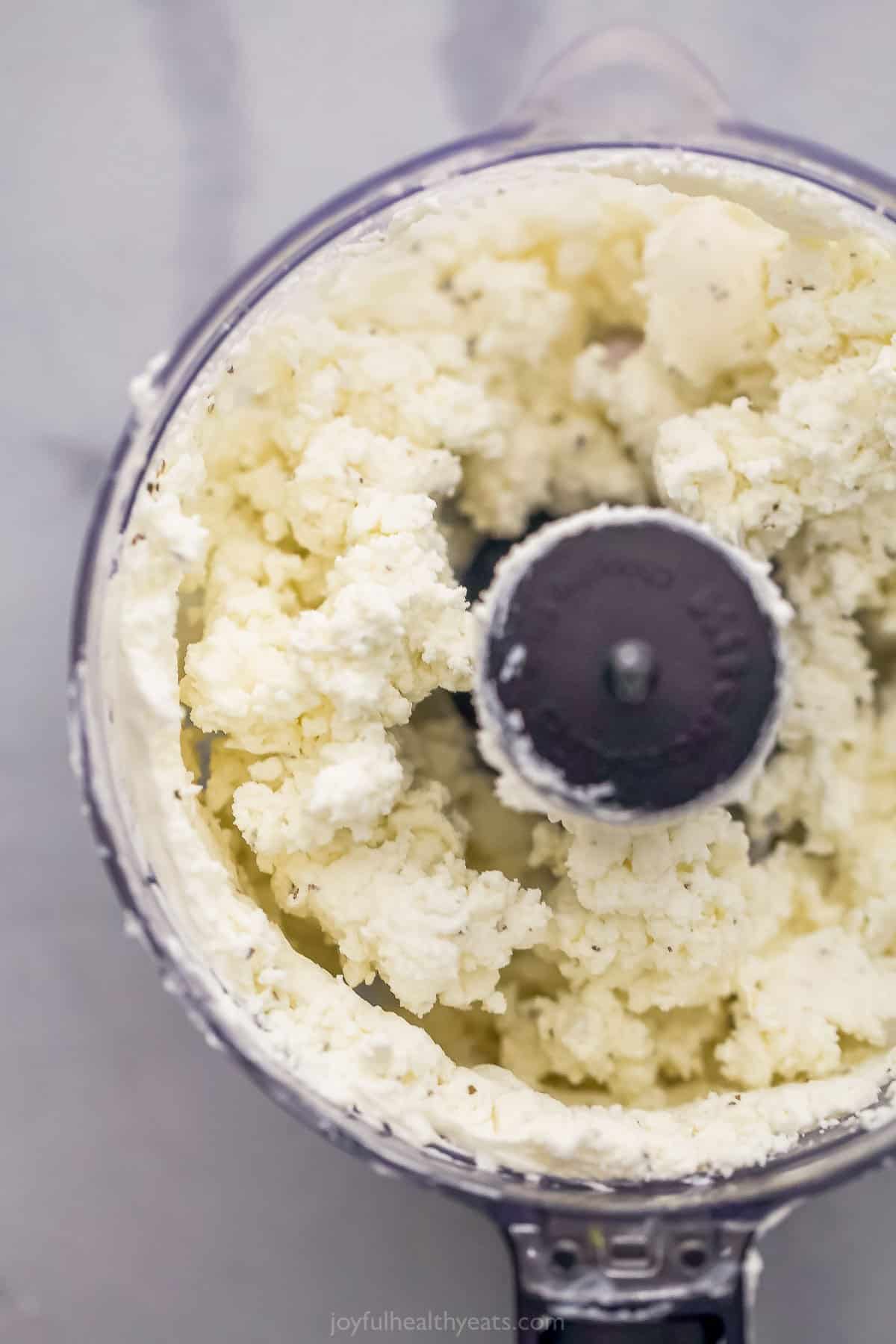 A food processor on top of a marble surface with the cheeseball mixture inside of it