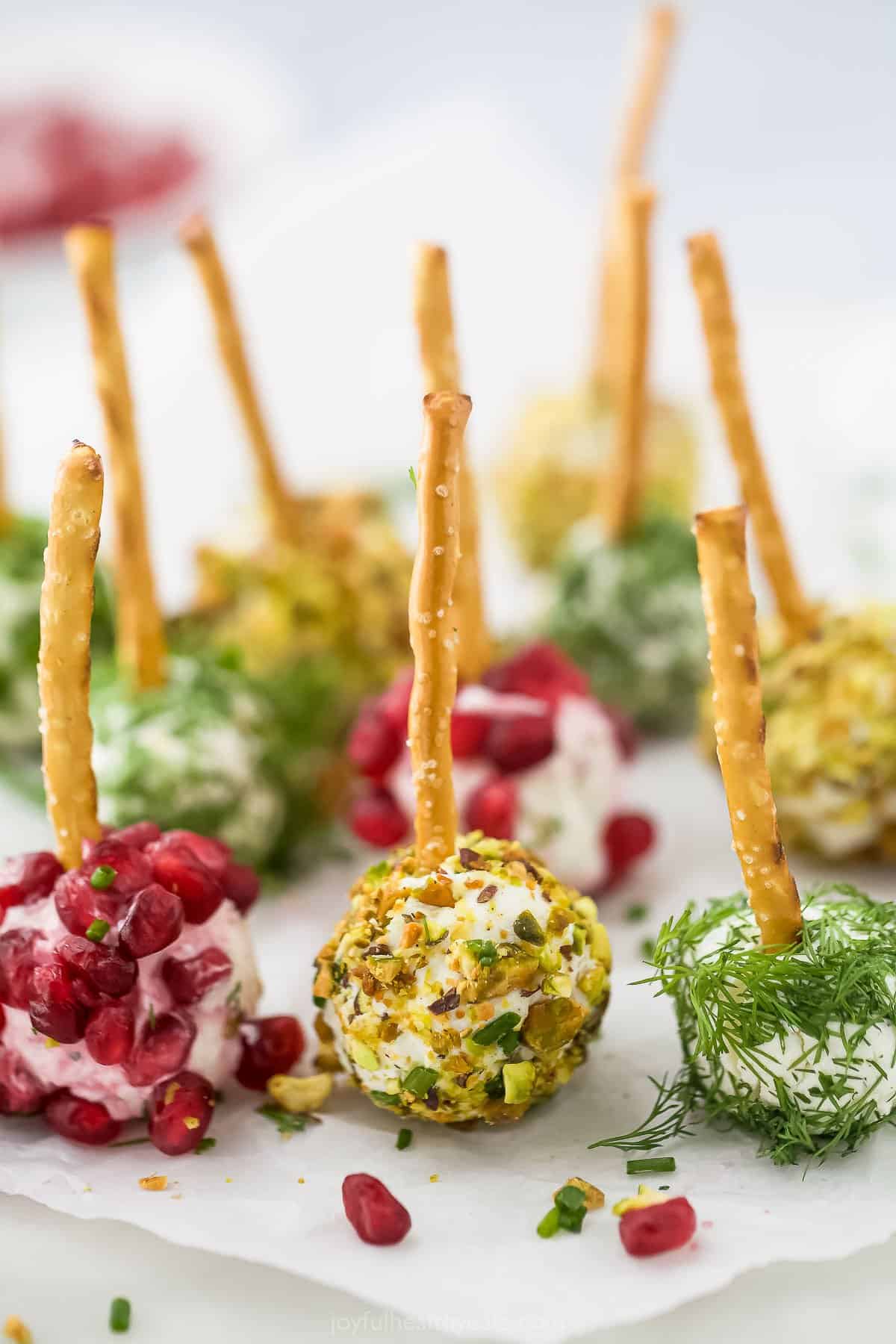 A bunch of different cheese balls with pretzels poking into them on a countertop