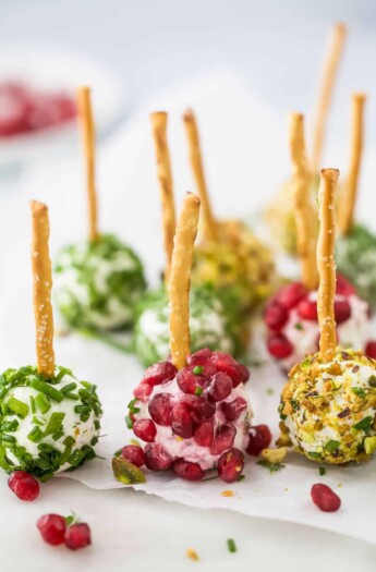 Nine assorted goat cheese balls on a sheet of parchment paper with a bowl of pomegranate seeds in the background