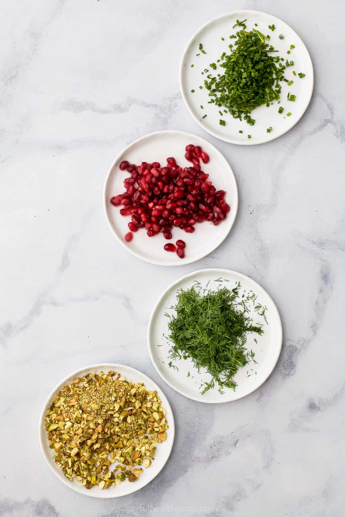 Four plates on a marble countertop with each one holding a different cheese ball topping