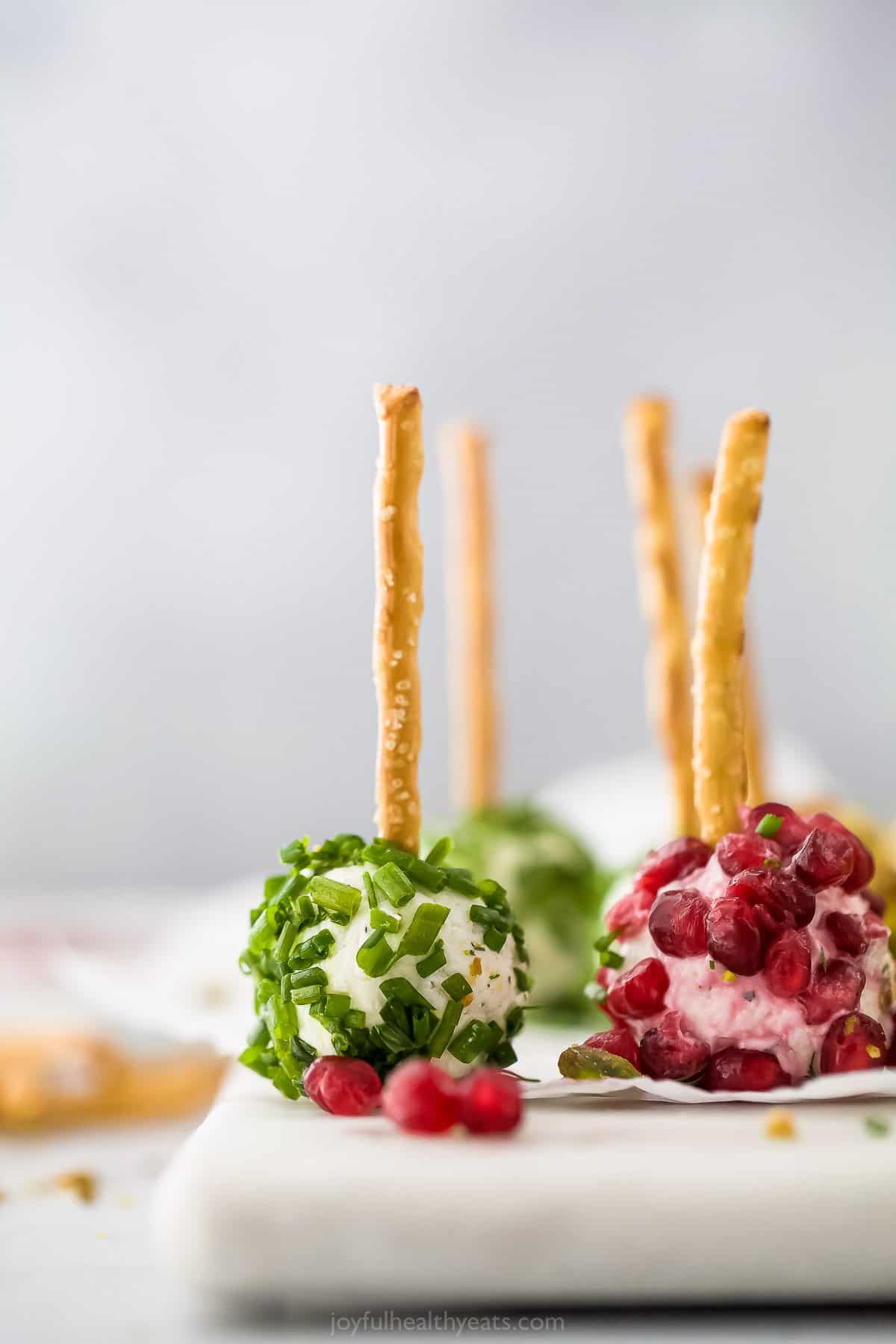 A pomegranate cheeseball beside a chive cheeseball on a plastic cutting board