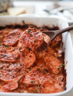 Scooping scalloped sweet potatoes out of a casserole dish.