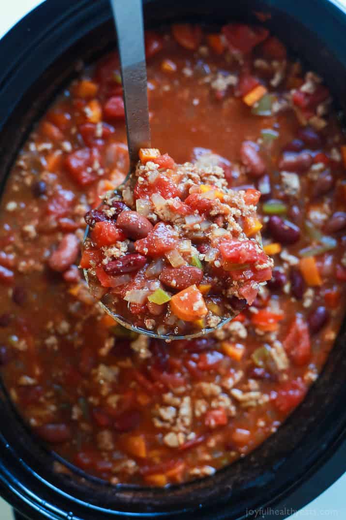 A ladle of turkey chili over a crockpot.