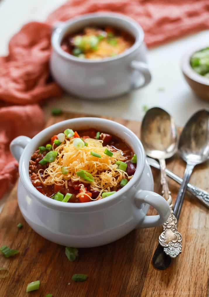 A cup of crockpot turkey chili topped with shredded cheese and green onions.