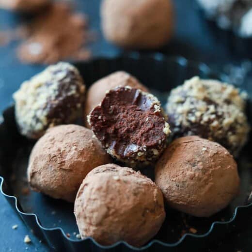 A bowl full of Decadent Healthy Chocolate Truffles with a bite taken out of one of them.