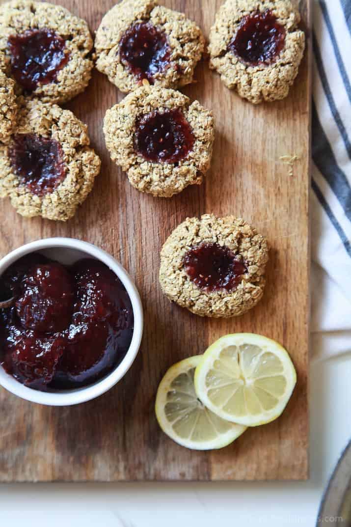 Top view of Flourless Lemon Raspberry Thumbprint Cookies on a cutting board with a dish of jam and lemon slices