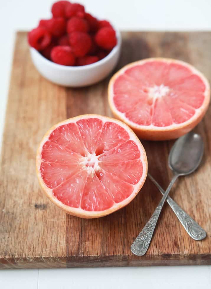 Two halves of grapefruit and a bowl of raspberries on a wooden board