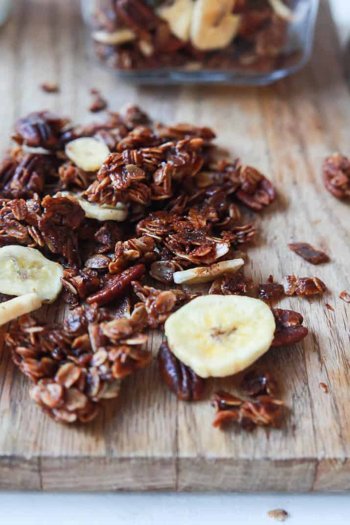 dark and roated granola with sliced of dried bananas on a wooden cutting board