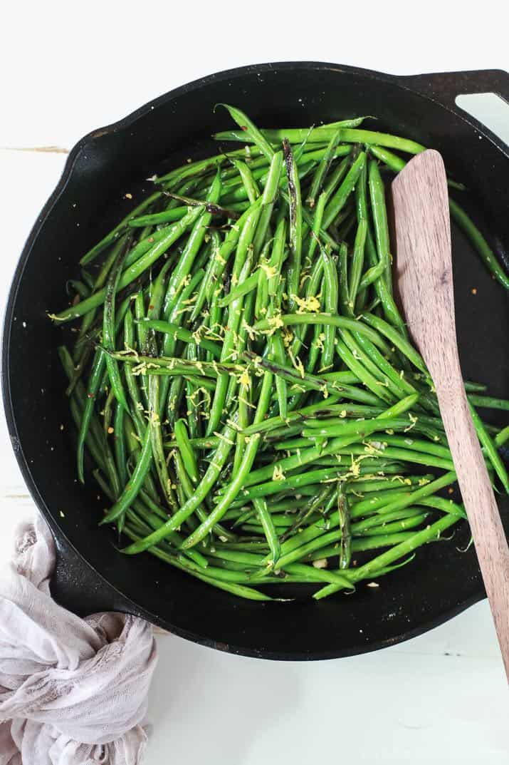 A Skillet Full of Green Beans Being Mixed with a Wooden Spoon
