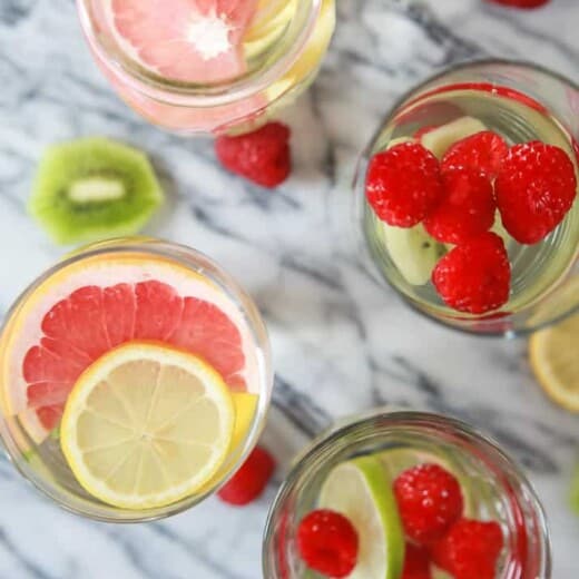 Overhead photo of glasses of fruit infused water with raspberries, lemon, limes, kiwi, and grapefruit.